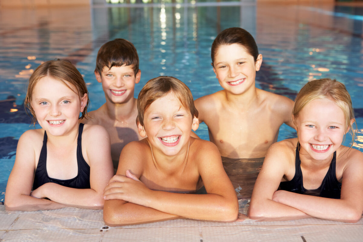 lachende Gruppe von Kindern am Beckenrand während Schwimmkurs