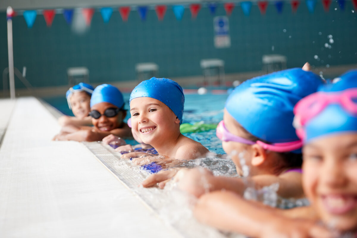 Lachende Kinder am Schwimmbeckenrand während Schwimmstunde